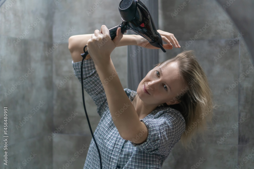 Young woman drying her blonde hair with a hair dryer in a stylish, modern bathroom, enjoying a refreshing morning routine filled with self-care and beauty practices