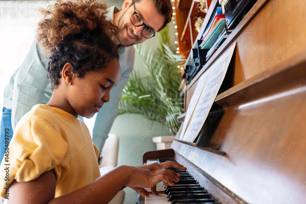 © NDABCREATIVITY - Happy man, pianist teacher giving piano lesson to a little school girl, playing music together
