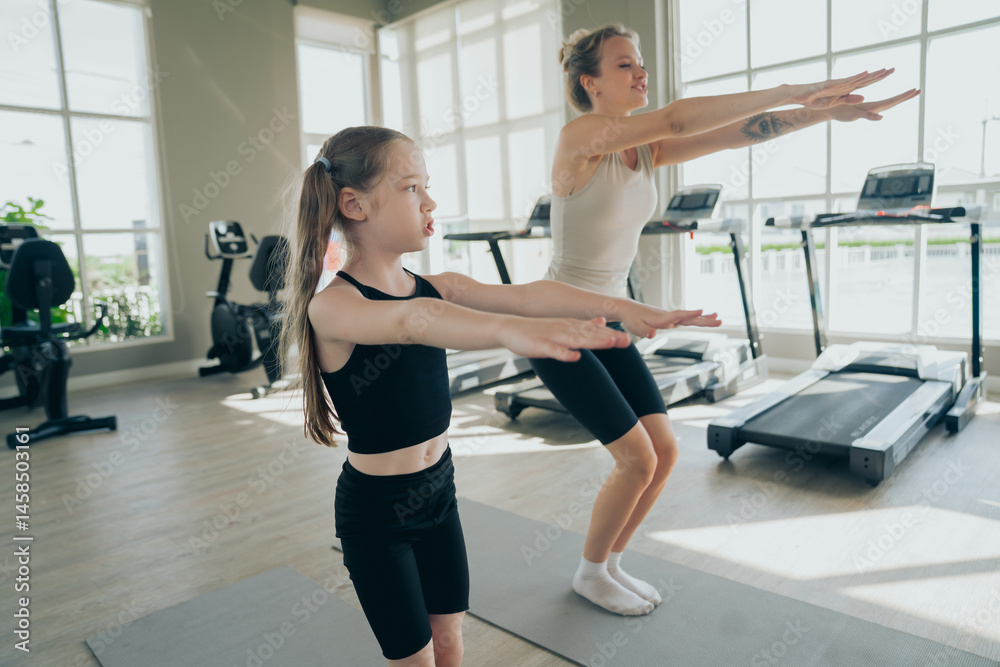 Fototapeta premium Beautiful girl and her cute little daughter smile while playing yoga, sport workout together at the gym