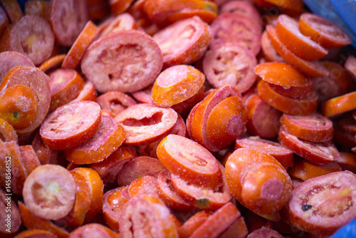 Obraz na płótnie Close-up of shock-frozen sliced red tomatoes with a thin ice coating. Are prepared for retail packaging to ensure extended shelf life in supermarkets and maintain perishable harvest quality. w salonie