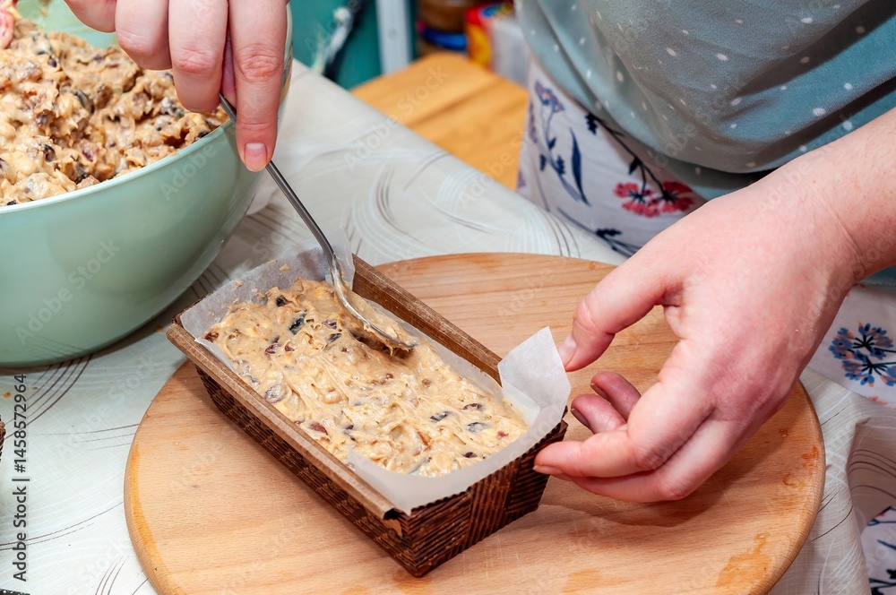 A person carefully fills a loaf pan with cake batter, getting ready to bake at home for a tasty treat.