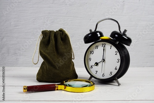 Time to Saving Concept money bag with alarm clock and magnifying glass on wooden background