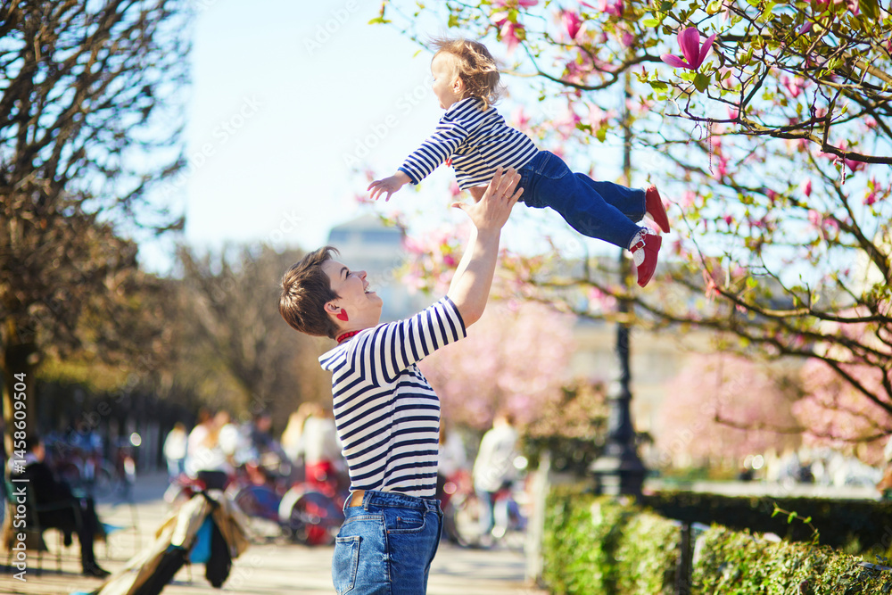 Fototapeta premium Beautiful young mother and her adorable toddler daughter walking together in park in Paris, France.