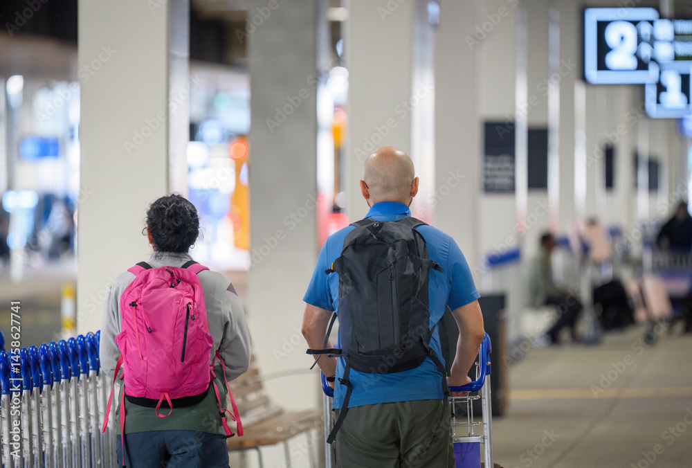 Passengers pushing luggage trolley at the airport.