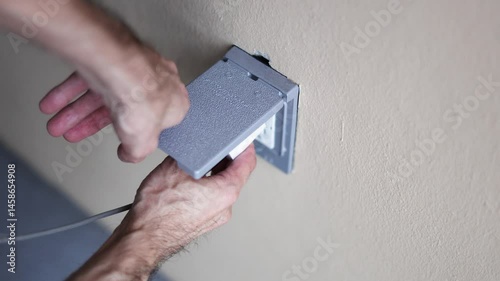 Close up of a hand holding a phone wall charger connect charger into outlet with cover outdoor