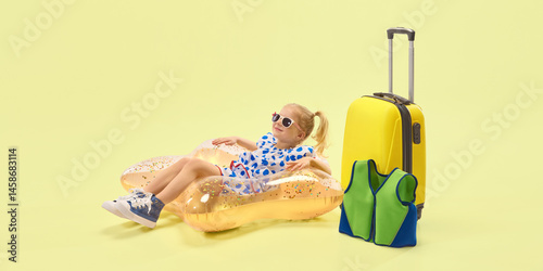 Obraz na płótnie Relaxed girl with ponytail hairstyle, in sunglasses lying on inflatable float beside suitcase joy against yellow background. Concept of childhood, summer vacation, travelling, trip w salonie