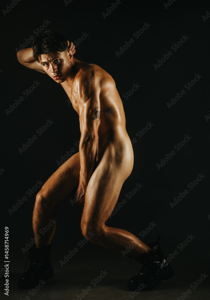 Naklejka premium A muscular man posing dramatically under low key lighting, emphasizing form and emotion.