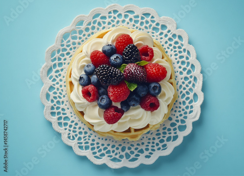 Obraz na płótnie waffles with cream and berries, on a white lace doily, against a blue background. Food photography, bright natural light,close-up of the waffles and fruit arrangement. w salonie