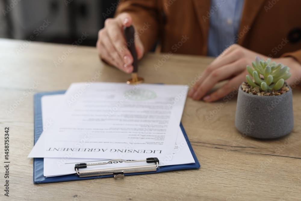 Obraz premium Woman stamping licensing agreement document at wooden table indoors, closeup