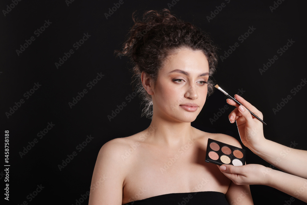 Obraz premium Makeup artist applying eyeshadows onto woman's face on black background, closeup. Space for text