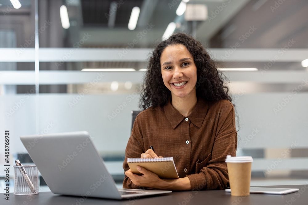 Portrait of successful satisfied businesswoman at workplace inside office. Woman smiling and looking at camera, holding notebook in hands, online conference meeting seminar. Portrait of successful satisfied businesswoman at workplace inside office. Woman smiling and looking at camera, holding notebook in hands, online conference meeting seminar.