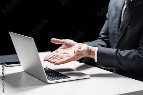 Businessman with a laptop holding or showing something in his hand. Cellphone and tablet on the table. Mockup and copy space. Business and technology concept
