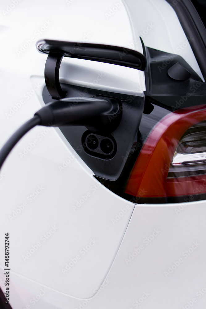 Electric car charging plug in rear tail light port of white sedan Electric car charging plug in rear tail light port of white sedan
