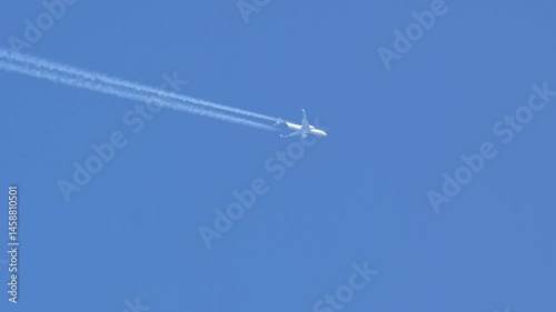 A passenger plane flies at cruising altitude and leaves long contrails behind it on a sunny day