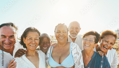 Happy senior people having fun walking on the beach at sunset wearing summer clothes - Joyful elderly lifestyle, vacation and travel concept - Main focus on center man face