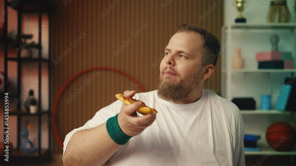 Overweight man eating pizza after home training, falling off diet with fast food