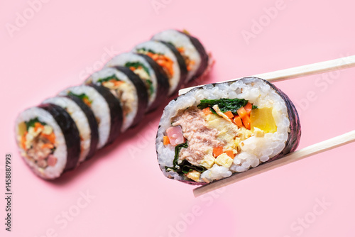 Wooden chopsticks with korean kimbap roll on pink background close-up.
