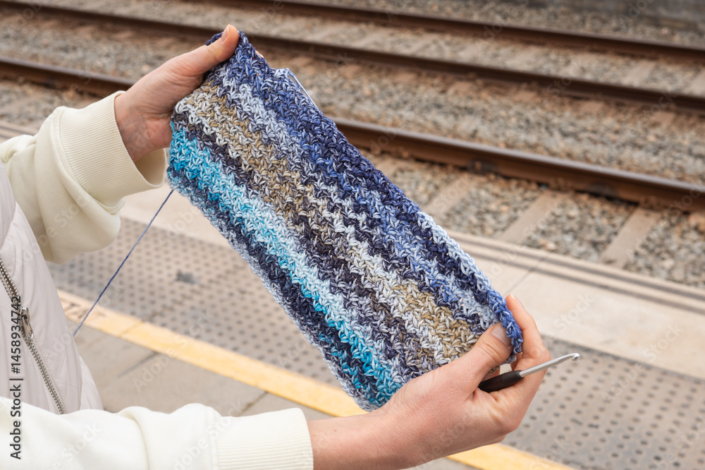 I Love Yarn Day. Female adult crocheting blue scarf at train station platform
