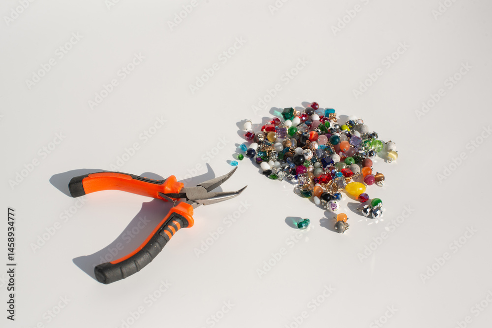 Orange handheld pliers and colorful beads on white background