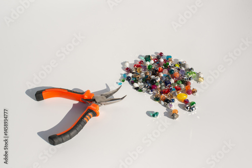 Obraz na płótnie Orange handheld pliers and colorful beads on white background w salonie