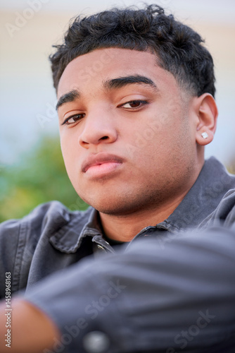 close-up portrait of a Dominican teenage boy wearing a shirt and earrings shows a suspicious or distrustful expression. Capturing the emotional complexity of adolescents transitioning into adulthood