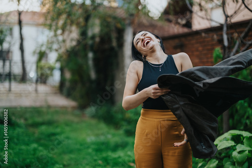 A happy woman laughing while interacting in an outdoor garden setting. She exudes cheerfulness and spontaneous energy. The scene is captured in a vibrant, lush environment with rich greenery.
