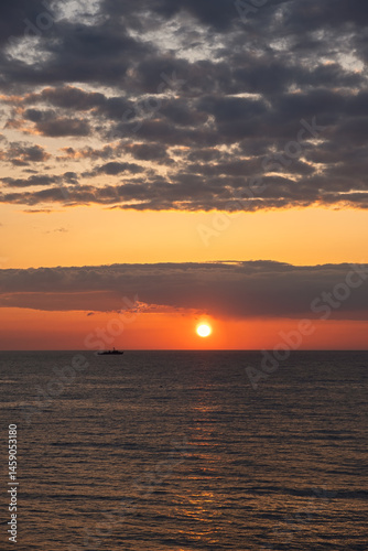 Orange sunset on the sea. Bright juicy landscape with feathery clouds on the horizon. Purple, lilac, pink shades of the evening sky. The smooth surface of the sea, a boat sails by. Idyll, relaxation