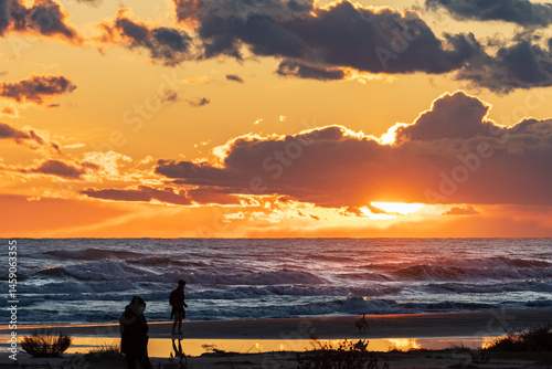 Silhouette people standing at beach against sky during sunset. Serene sunset over Ribes Roges beach, Vilanova. Soft waves and golden light create a peaceful scene.