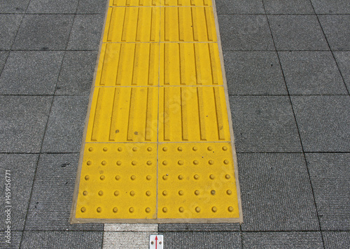 Yellow blocks of tactile paving for blind handicap. Tactile pavement for the visually impaired close up background. Texture of square gray paving tile with Braille blocks in the street.