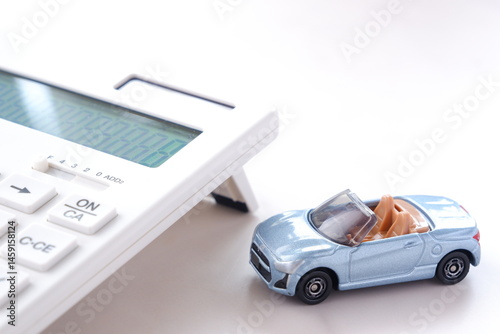 電卓と自動車のミニチュア模型で、車検など高騰する自家用車の維持費の負担に頭を悩ましているイメージ