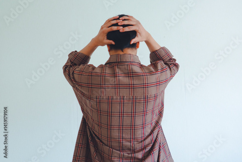 Stressed Asian man grabbing his head from behind, showing frustration and anxiety on isolated white background, emotional back view pose