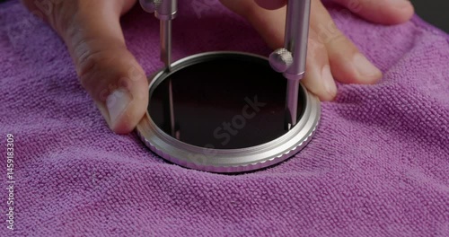A worker unscrews the holder from variable ND filter to disassemble it and clean glass inside. Close-up.