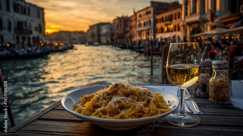 Photograph of a romantic dinner with pasta and champagne on the table in a restaurant near a window overlooking a canal in Venice, Italy.