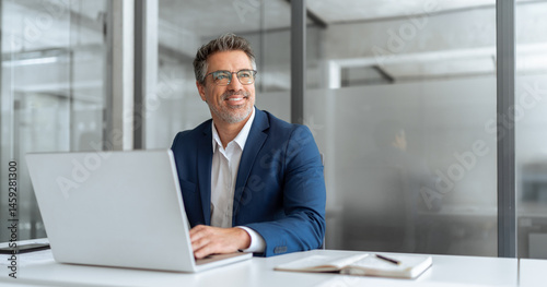 Middle age latin male entrepreneur businessman working on financial sale work at desk in office. Mature indian business man in suit using pc laptop for trading, looking smiling, dreaming at copy space