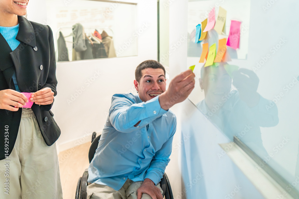 Young businessman in wheelchair sticking notes on a whiteboard during a meeting with a female colleague