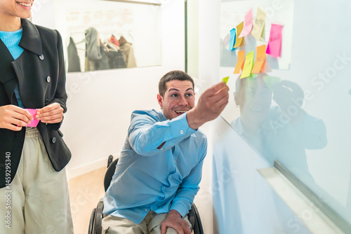 Obraz na płótnie Young businessman in wheelchair sticking notes on a whiteboard during a meeting with a female colleague w salonie