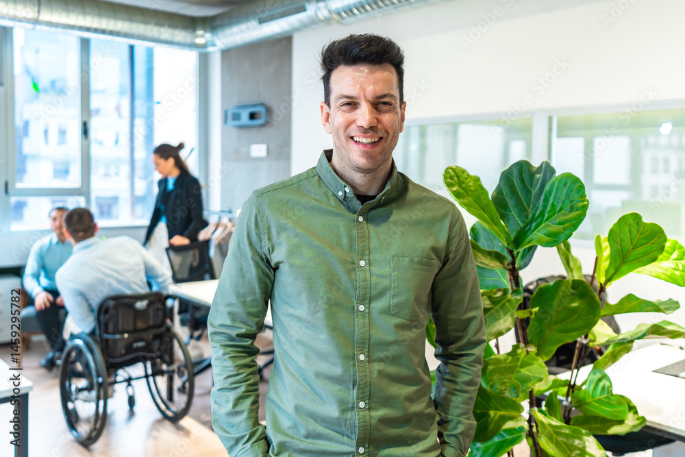 Confident businessman smiling in modern inclusive office with disabled colleagues working