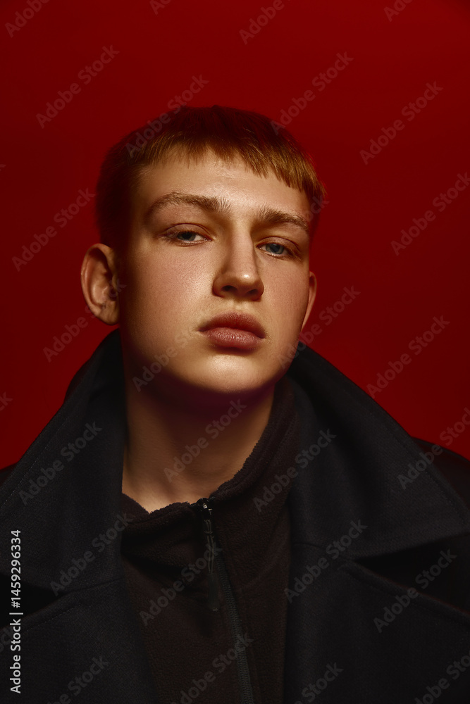 Close-up portrait of young confident man wearing dark jacket, posing against deep red background, looking directly at camera. Concept of bold fashion, style, youth culture, self-expression
