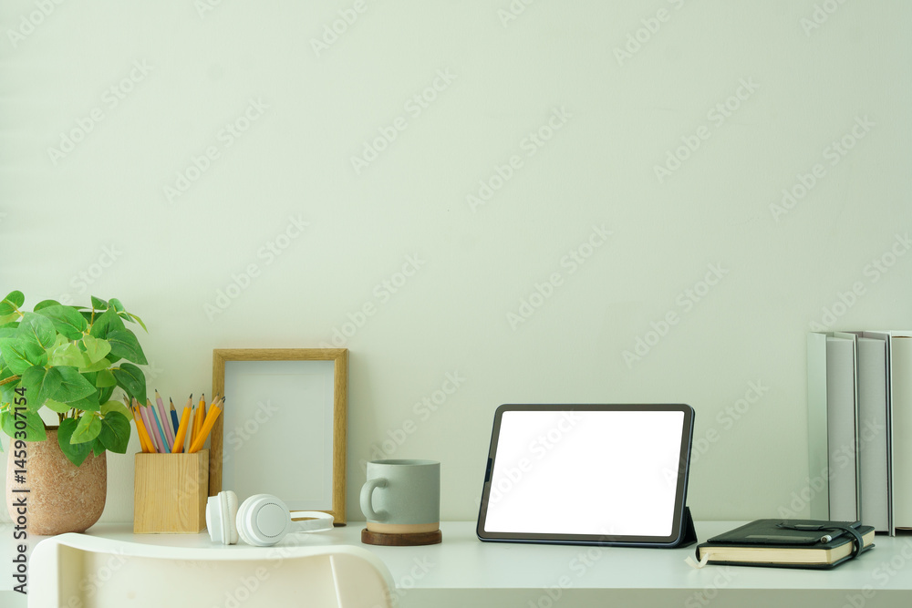 Fototapeta premium Creative workspace with blank tablet screen, framed photo and potted plant, ideal for showcasing productivity, or website mockups.