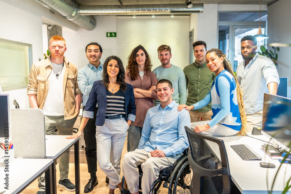 Diverse business team posing with disabled colleague in wheelchair in modern office