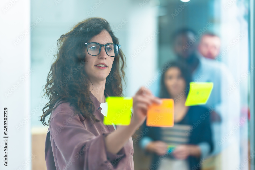 Young manager planning strategy using sticky notes on glass wall in office meeting room