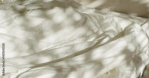 Sunlight streams through a window, casting dancing shadows of leaves on an unmade bed. The soft, white linens invite relaxation and rest. Perfect for lifestyle, home decor, or sleep-related projects.