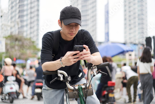 portrait of young Asian man using smartphone when riding bike on street