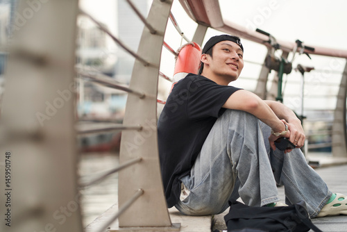 handsome young Asian man sitting beside his bike at waterfront smiling photo