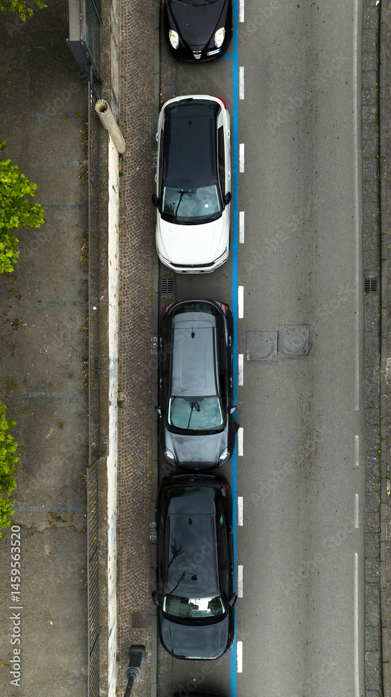 Aerial zenithal view on a narrow street with parked cars. This urban road is located in Italy.