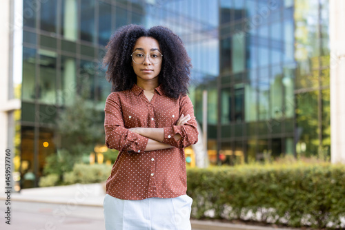 Obraz na płótnie A confident business woman stands outdoors with arms crossed, with a modern building behind her. She is wearing glasses. w salonie
