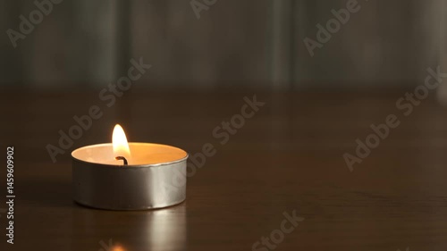 A small candle flickers softly while sitting on a wooden table. The warm glow fills the dimly lit room, creating an inviting atmosphere for relaxation.