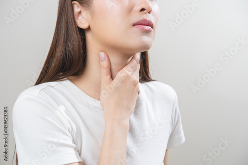 Sickness in inflaming asian young woman, girl use hand check self touch at sore throat, pain thyroid gland on neck or disease reflux, acid of suffer people on wall background. Medical and healthcare.