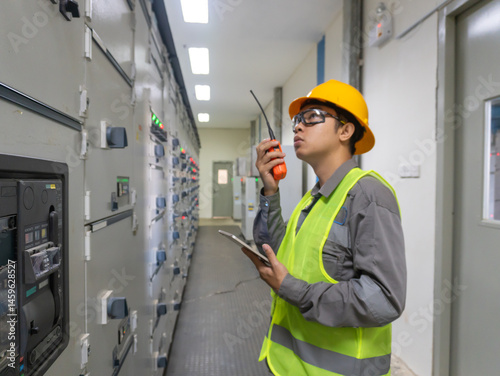 Portrait Asian Young Man, Working as an Engineer at a Power Plant Facility, Wearing a Work Jacket, Safety Glasses, and a Yellow Hard Hat. Electrical industry specialist Working on a Tablet Computer
