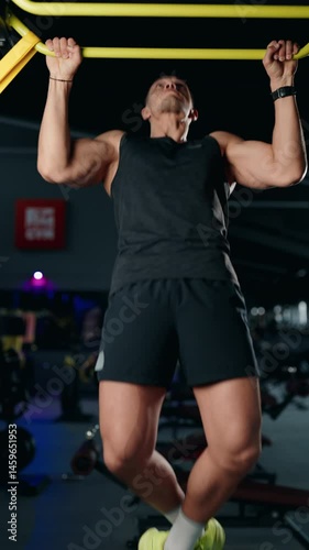 Muscular man doing pull-ups in a modern gym. He demonstrates strength, fitness, and determination as he completes each repetition. The gym environment adds to the energetic atmosphere.